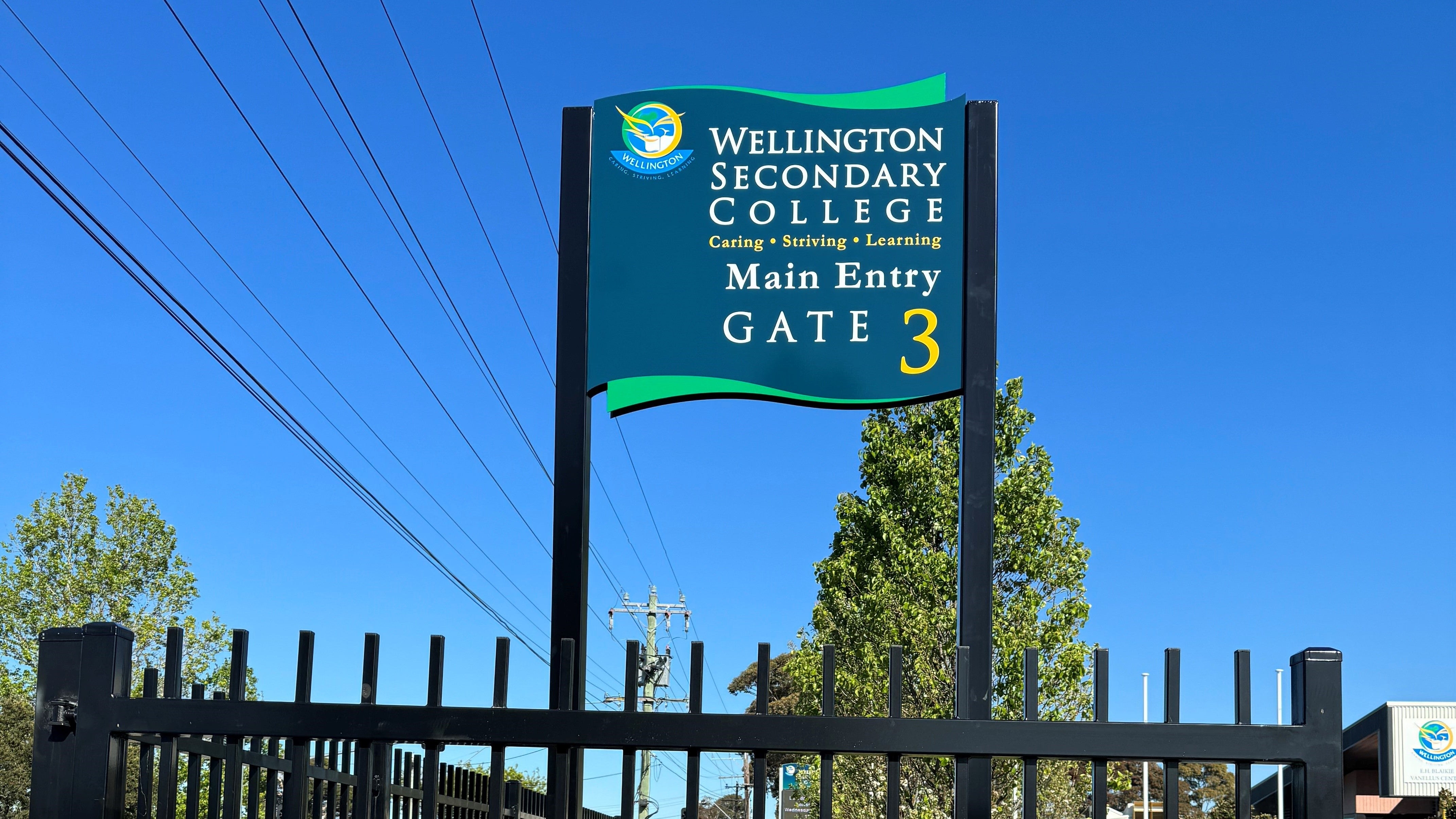 School gate with a sign indicating 'Wellington Secondary College Main Entry Gate 3' on a clear day.